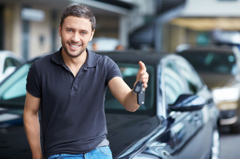 A man in a black polo shirt smiles, holding car keys