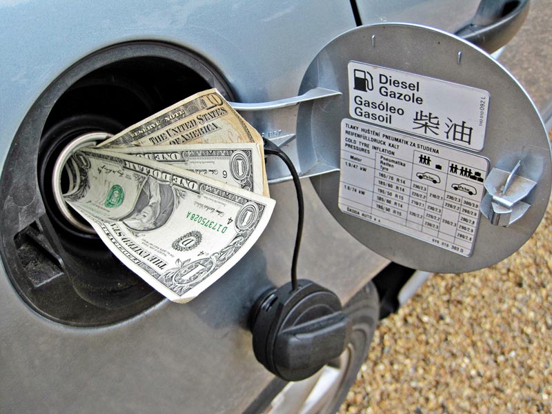 An open car fuel cap with several U.S. dollar bills inserted